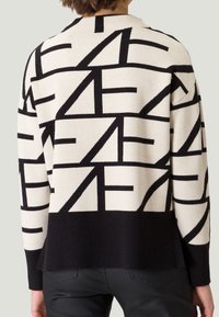 Gebreide trui in beige met gedurfde zwarte abstracte patronen. Geribbelde zoom en manchetten; ontspannen pasvorm met een ronde halslijn en zij-splitten.