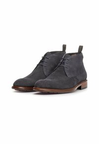 Botas chukka de color gris oscuro con una parte superior texturizada, cordones y una lengüeta, con una suela de cuero suave y un tacón bajo.