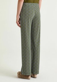 Pantaloni a gamba larga con motivo verde decorati da un design geometrico in viola e bianco. Tessuto liscio con una texture sottile.