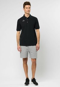 Zwarte polo met korte mouwen en een kraag, met een klein wit logo. Gecombineerd met grijze katoenen shorts en zwarte sportschoenen.