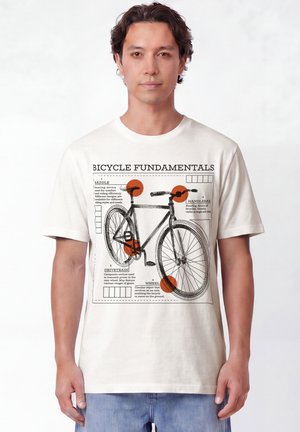 Mann trägt weißes T-Shirt mit detailliert beschriftetem schwarzem Fahrraddiagramm und orangen Kreisen zur Hervorhebung wichtiger Teile.