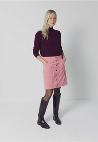 Collo blu melanzana abbinato a una gonna in velluto a coste rosa con bottoni frontali e tasche, completato da stivali neri fino al ginocchio.