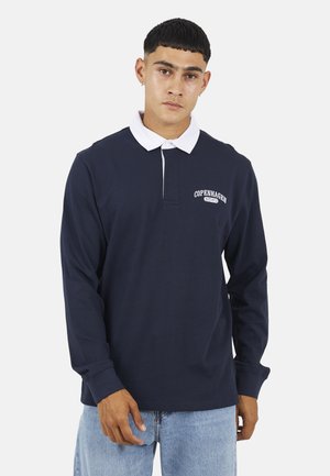 Marineblauwe polo met lange mouwen en een witte kraag, voorzien van een borstlogo met de tekst "COPENHAGEN EST 1970." Gemaakt van katoen met een gladde textuur.