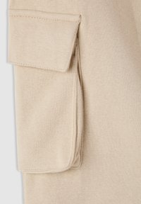 Beżowa bawełniana tkanina z boczną kieszenią; gładka faktura z starannym szwem. Klapy kieszeni mają kwadratowe rogi. Prosty design.