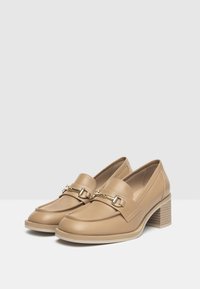 Beige leren loafers met een chunky hak, voorzien van een decoratieve gouden kettingaccent en een gestructureerde loopzool. Klassiek ontwerp met een ronde neus.