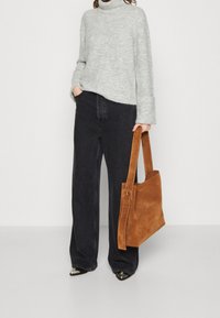 Grå stickad turtleneck-sweater, svarta vida jeans och en brun mocka tote-väska. Ensembeln har en avslappnad passform och glänsande svarta skor.