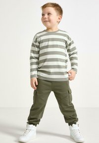 Gestreepte grijs-witte longsleeve shirt gecombineerd met olijfgroene cargo broek en witte sneakers met banden. Casual, lichtgewicht stof.