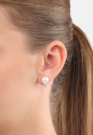 Un paio di orecchini a perno che presentano una perla bianca e una piccola pietra trasparente. Metallo tono argento con una finitura liscia e lucida.