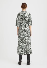Robe longue et fluide avec un imprimé feuillé vert et blanc, cintrée à la taille, dotée de manches flottantes et d'un ourlet volé.
