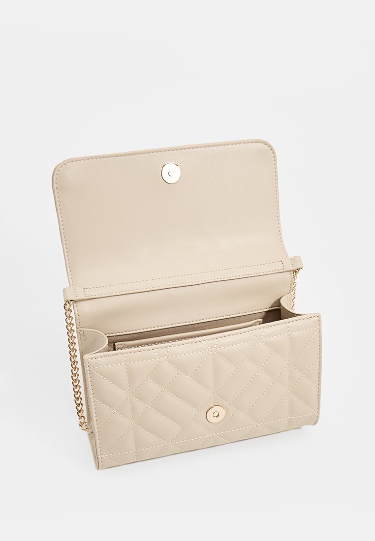 Bolso de mano de imitación cuero color beige con patrón acolchado, herrajes dorados, cierre de botón magnético y correa de cadena; el interior cuenta con múltiples compartimentos.