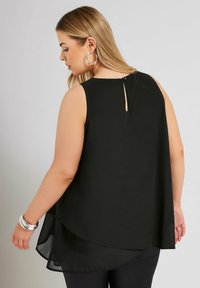 Svart ärmlös topp med en rundad nederkant, lätt tyg och en liten nyckelhåldetalj på baksidan, parat med silverfärgade hoops. 