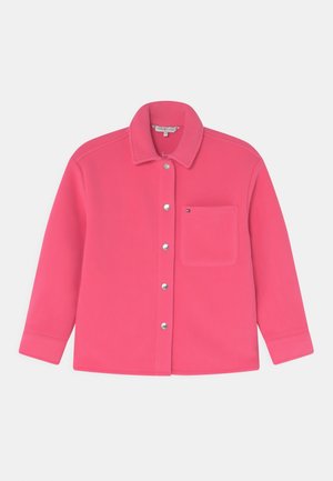 Różowa polarowa kurtka z kołnierzykiem, z przodu zapinana na guziki i z jedną kieszenią na piersi. Posiada srebrne elementy metalowe oraz gładką fakturę.