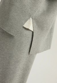 Jasnoszary sweter z bocznym rozcięciem i kontrastującym kremowym materiałem z dołu. Miękka tekstura z prążkowanymi brzegami dla dodatkowego szczegółu.