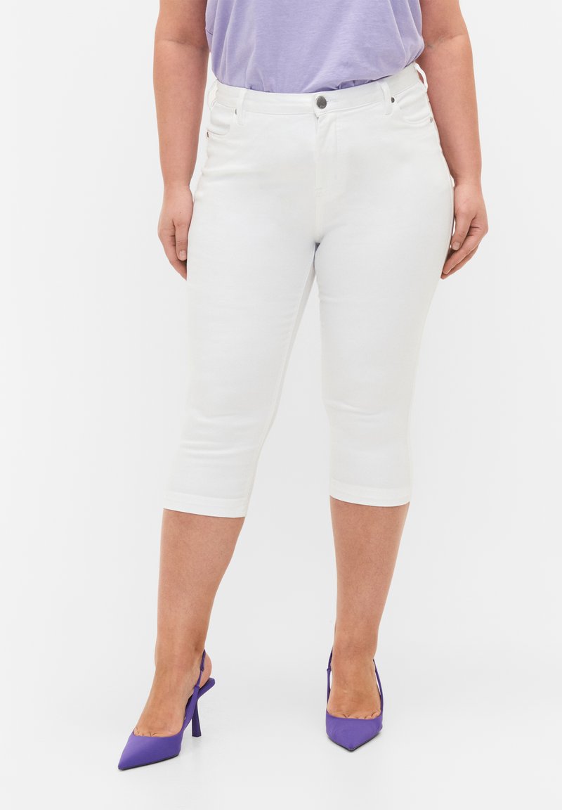 Jeans blancos recortados con una silueta ajustada, que presentan un diseño de cinco bolsillos y costuras en contraste. Combinados con zapatos de tacón altos morados.