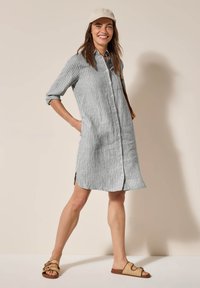 Vestito camicia a righe grigie e bianche con maniche lunghe, bottoni, fessure laterali, realizzato in materiale leggero, abbinato a sandali scivolati beige.