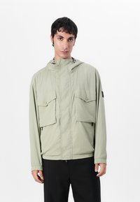 Light green hooded jacket with two large chest pockets and elastic cuffs. Made from lightweight material with a smooth texture.