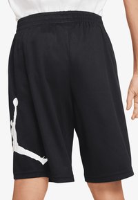 Pantalones cortos de baloncesto de malla negros con una cinturilla elástica y un gran gráfico blanco de un jugador en el aire en la pierna izquierda.