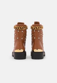 Bottes chevilles en cuir marron avec un design matelassé, bordure en chaîne dorée et accents en strass. Semelle épaisse en caoutchouc noir avec détail de logo au talon.