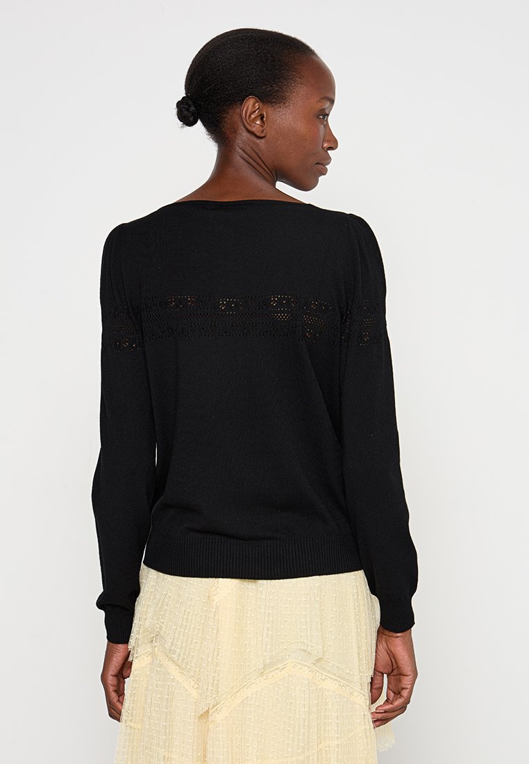 Schwarzer Strickpullover mit rundem Halsauschnitt, voluminösen langen Ärmeln und einem zarten gemusterten Rückenteil. Weiche Textur und taillierter Saum.