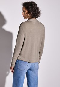 Haut à manches longues vert olive clair avec un éclat subtil, coupe décontractée et ourlet arrondi, assorti à un jean taille haute bleu clair à jambes larges.