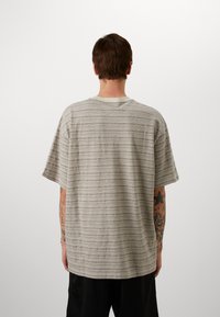 Light gray short-sleeve t-shirt with horizontal stripes, featuring a round neckline and a relaxed fit. Fabric appears textured and casual.