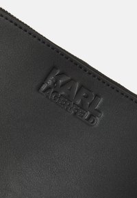 Pochette en cuir noir avec logo embossé "KARL LAGERFELD" et couture visible de la fermeture éclair le long du bord supérieur.