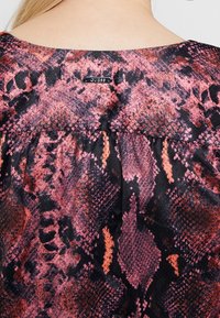 Bunte Bluse mit einem pinken und schwarzen Schlangenhautmuster, weichem Stoff, runder Ausschnitt und einem kleinen Markenetikett auf der Rückseite.