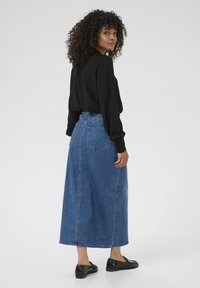 Denim maxi skirt with a high waistband and back pockets. The fabric is medium blue with a smooth texture. Black flat shoes worn.