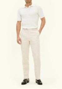 Vit stickad polo med krage, beige skräddarsydda byxor och svarta lackskor, vilket ger en formell men ändå avslappnad look.
