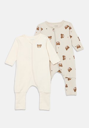 Dois bodies de bebé. Um é creme claro com uma imagem de um urso; o outro é bege com padrões repetidos de urso e pegada. Mangas compridas, fecho de correr.