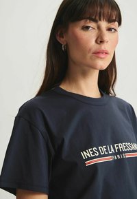 T-shirt en coton bleu marine avec un design graphique portant le texte "INES DE LA FRESSANGE PARIS" et des accents rouges sur le devant.