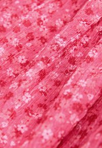 Roze bloemenstof met een zachte textuur, voorzien van kleine witte en donkerroze bloemen op een licht gekreukeld oppervlak.