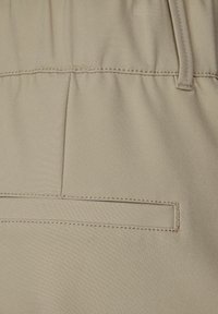 Pantaloni beige con una texture liscia, dotati di tasca posteriore con cuciture nascoste e di una cintura elastica per il massimo comfort.