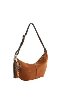 Sac à main en daim marron en forme de croissant avec bandoulière réglable foncée, fermeture éclair dorée et breloque à pompon perlée suspendue sur le côté.