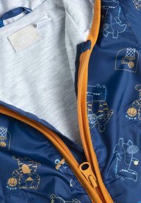 Chaqueta acolchada con un exterior azul marino, ilustraciones coloridas de animales, ribete naranja en el cierre y un forro interior gris.