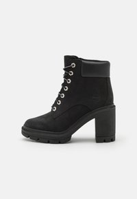 Black suede ankle boots with a chunky high heel, lace-up design, silver eyelets, and a padded collar for comfort. Rugged sole texture.