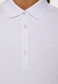 Witte polo shirt met een kraag, vier knopen, verticale ribbeltextuur en een subtiel geborduurd logo aan de linkerkant.