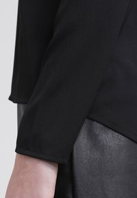 Zwarte lange mouw top gemaakt van een zachte, lichte stof. Heeft een comfortabele pasvorm en omgeslagen mouwen, gecombineerd met een gestructureerde zwarte leren rok.