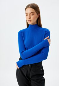 Langärmliges Rollkragenoberteil in strahlendem Blau, aus einem dehnbaren Stoff gefertigt. Verfügt über ein tailliertes Design mit verlängerten Ärmeln und glatter Textur.