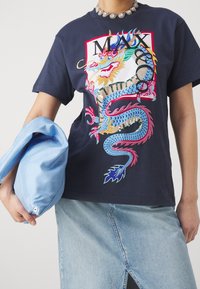 Granatowy bawełniany t-shirt z kolorową grafiką smoka i napisem „MAX”. Modelka trzyma jasnoniebieską torbę, mając na sobie spódnicę dżinsową.