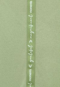 Green fabric with a textured finish, featuring a vertical ribbon that has white printed text: "grateful < magnificent moments."