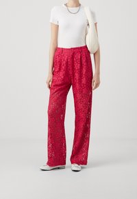 Röda spetsbyxor med blommönster, löst sittande och vida ben. Matchas med en vit t-shirt och vita skor. Enkel kedja i halsbandet och väska.