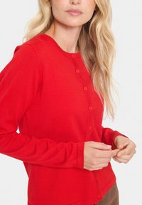 Cardigan rouge à manches longues avec un col rond, devant boutonné et texture douce. Présente des boutons assortis et des manches ajustées.