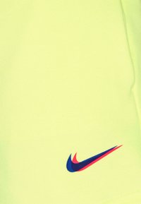 La tela amarilla brillante de Nike presenta una textura suave, con un logo de swoosh azul y rojo en la esquina inferior derecha.