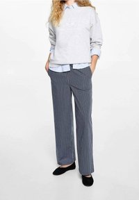 Šedá mikina s nápisem "Long Island", přes kterou je lehká modrá košile s límečkem. Modro-bílé pruhované široké kalhoty, černé baleríny.