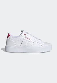 Vita sportssko med texturerad syntetisk överdel, röda detaljer, perforerad design, platt sula och snörningsstängning. Varumärkeslogotyp på sidan.