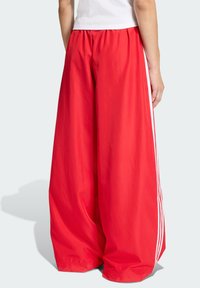 Pantalones rojos de pierna ancha hechos de material ligero, con franjas blancas laterales, cintura elástica y una textura suave.