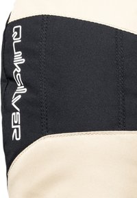Schwarzes und beiges Stoffpaneel mit geschwungener Form. Enthält ein auffälliges weißes Quiksilver-Logo. Glatte Oberfläche und sichtbare verstärkte Nähte.