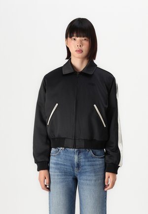 Black bomber jacket with a zip front, ribbed cuffs, and white stripe accents. Soft fabric with side pockets and a classic collar style.