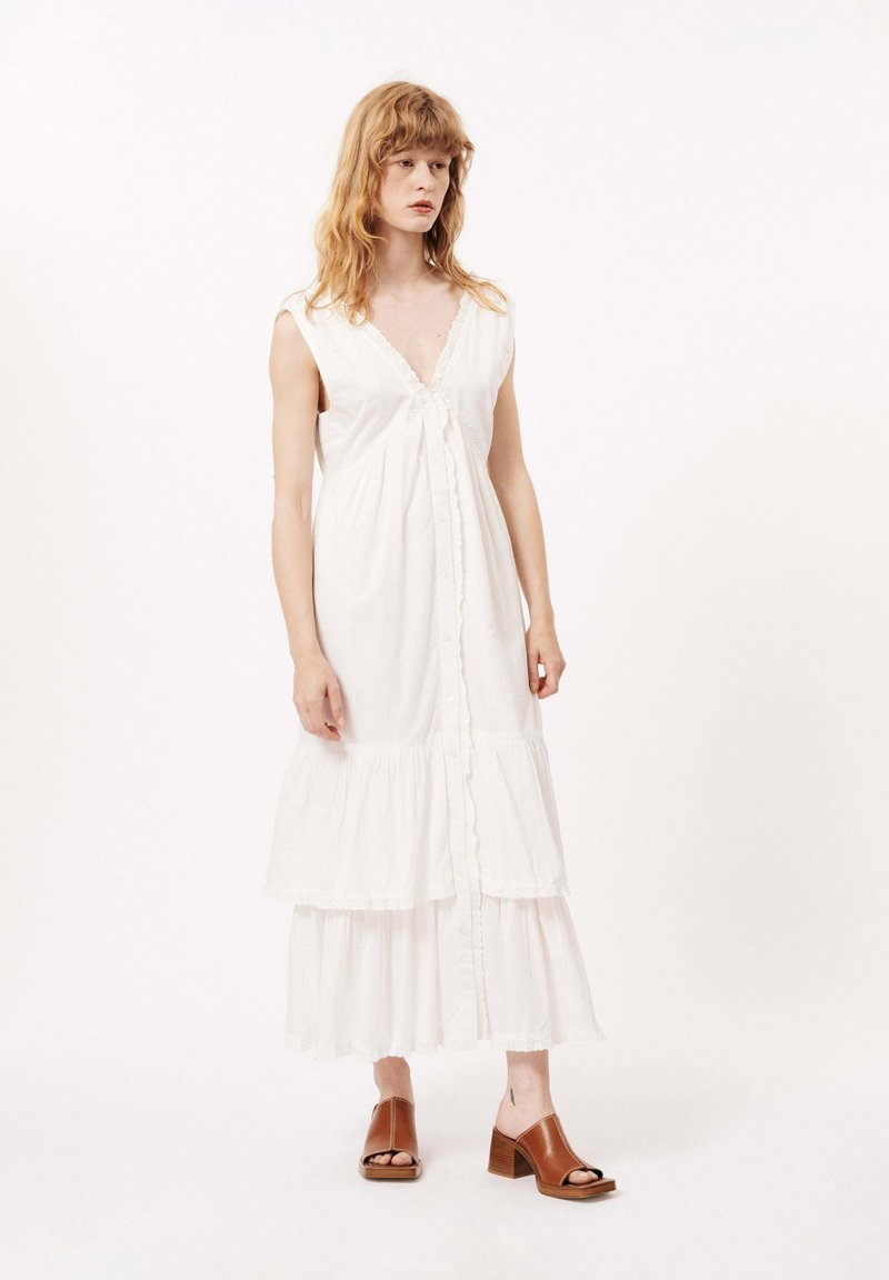 Robe midi blanche à étages avec un décolleté en V, fermeture à boutons et bordure en dentelle, fabriquée en tissu léger. Associée à des sandales à talons carrés marron.